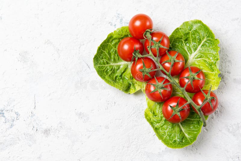 Pomodori di ciliegia rossa maturati sulla lattuga principale foglie di pietra vista in alto con spazio di copia fotografie stock