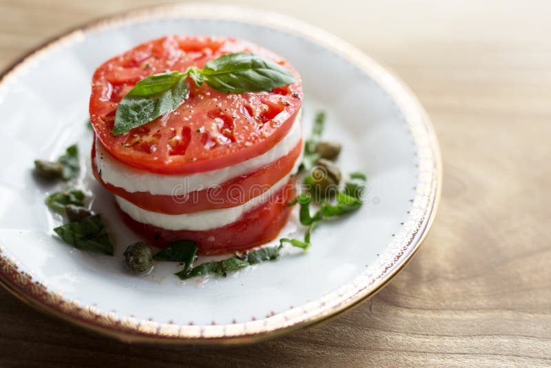 Pomodoro a fette e formaggio di mozzarella in un'insalata di caprese con basilico fresco e cappucci fotografia stock Pomodoro a fette e formaggio di mozzarella in un'insalata di caprese con basilico fresco e cappucci fotografia stock