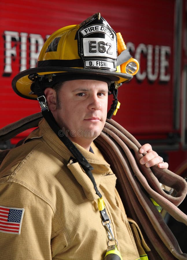 Brave portrait of a firefighter standing in front of fire engine in uniform holding a fire hose. Brave portrait of a firefighter standing in front of fire engine in uniform holding a fire hose