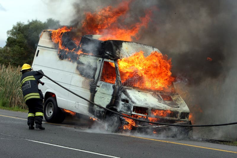 Burning motor vehicle been put out by firemen in protective clothing. Burning motor vehicle been put out by firemen in protective clothing