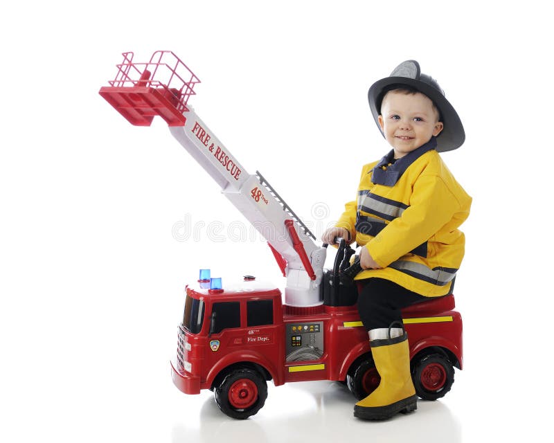 An adorable toddler happily playing fireman on his toy fire truck. On a white background. An adorable toddler happily playing fireman on his toy fire truck. On a white background.