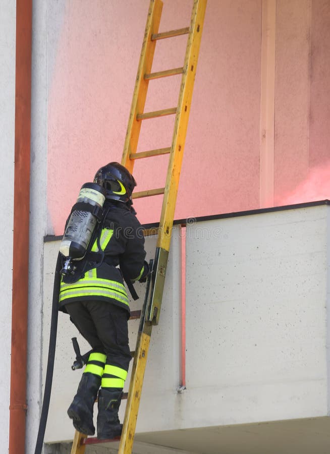 Pompiere con il cilindro di ossigeno che sale una scala di legno fotografia stock libera da diritti Pompiere con il cilindro di ossigeno che sale una scala di legno fotografia stock libera da diritti