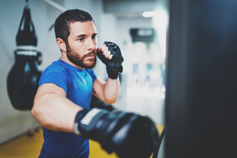 Pontapés praticando kickboxing musculares novos do lutador com saco de perfuração Retroceda o encaixotamento do pugilista como o fotos de stock royalty free Pontapés praticando kickboxing musculares novos do lutador com saco de perfuração Retroceda o encaixotamento do pugilista como o fotos de stock royalty free