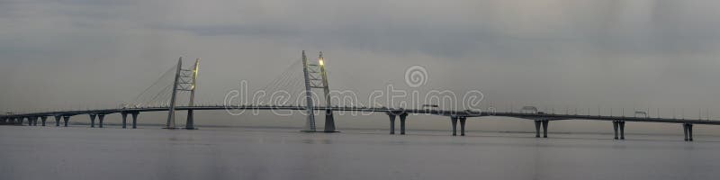 Panoramic view: high cable-stayed bridge over the bay in the evening twilight. Panoramic view: high cable-stayed bridge over the bay in the evening twilight