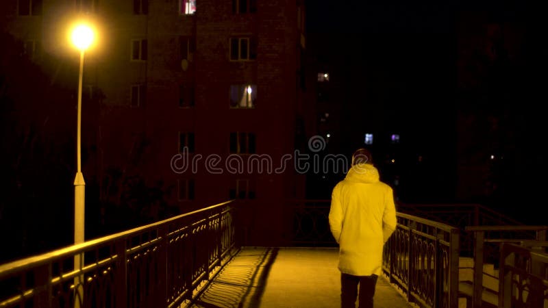 Ponte pedonale con una lampadina solitaria e un uomo che la attraversa di notte Riprese in borsa Veduta posteriore di un giovane