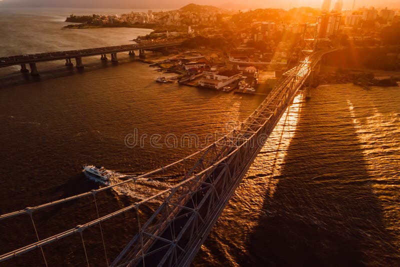 Old cable bridge with sunset light and touristic boat in Florianopolis, Brazil. Aerial view. Old cable bridge with sunset light and touristic boat in Florianopolis, Brazil. Aerial view