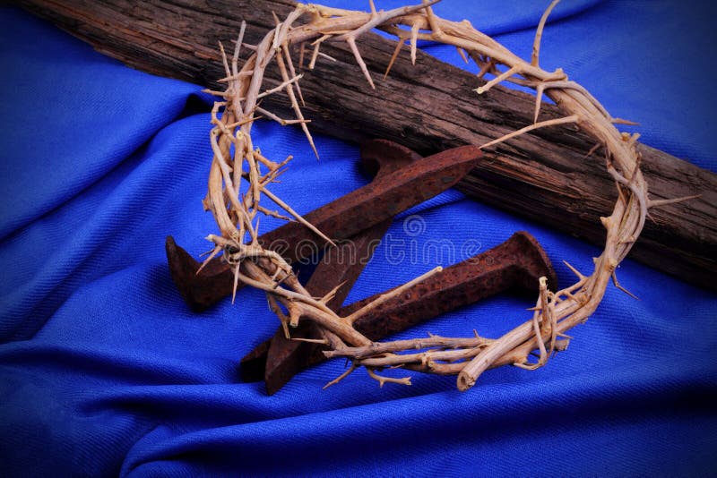 A woven crown of thorns, rusty spikes with a rustic timber on a blue woven cloth. Used in the Crucifixion of Jesus in Jerusalem. Easter symbols. A woven crown of thorns, rusty spikes with a rustic timber on a blue woven cloth. Used in the Crucifixion of Jesus in Jerusalem. Easter symbols.