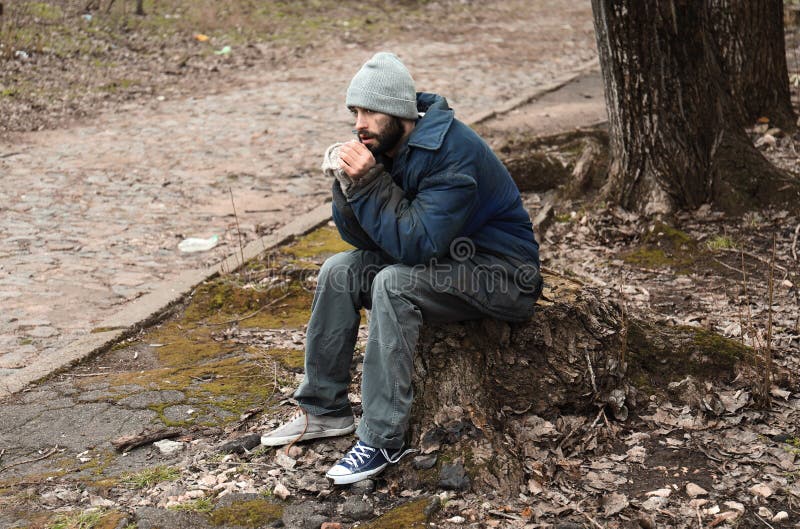 Poor homeless man sitting on stump stock photo