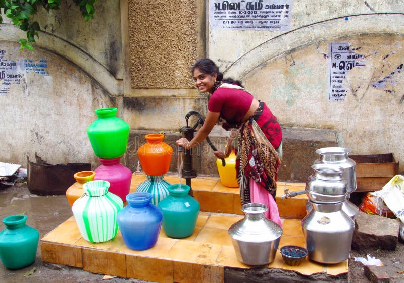 Poor young Indian woman in a sari with colorful pots near the water source