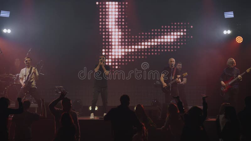 Pop group performs in front of cheering crowd on stage with bright multicolored lights. Live concert. Slow motion stock video footage