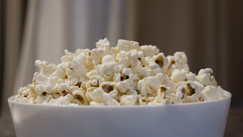 Popcorn in una ciotola bianca davanti a fondo vago fotografie stock Popcorn in una ciotola bianca davanti a fondo vago fotografie stock