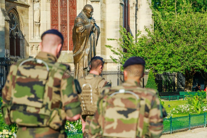 PARIS, FRANCE - JULY 1, 2017: Pope John Paul II statue guarding soldiers of National Armed Forces in Notre Dame of Paris, keeping security after recent terrorist attacks in Paris. PARIS, FRANCE - JULY 1, 2017: Pope John Paul II statue guarding soldiers of National Armed Forces in Notre Dame of Paris, keeping security after recent terrorist attacks in Paris.