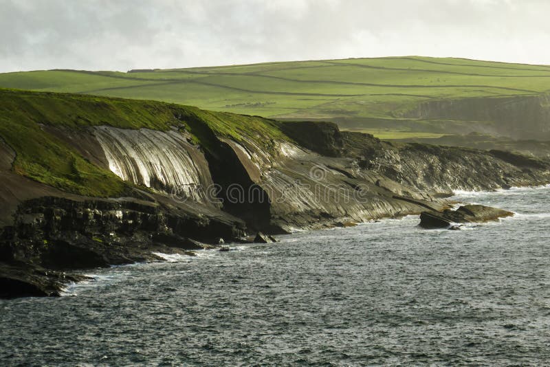 Popołudniowy słońce shimmers na mokrych mechatych Kilkee falezach wzdłuż Dzikiego Atlantyckiego sposobu, okręg administracyjny Cl fotografia stock Popołudniowy słońce shimmers na mokrych mechatych Kilkee falezach wzdłuż Dzikiego Atlantyckiego sposobu, okręg administracyjny Cl fotografia stock