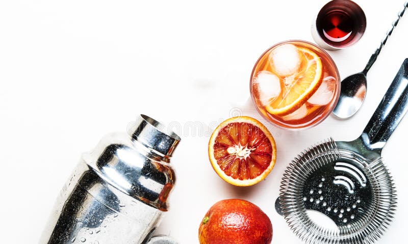 Popular alcoholic cocktail Negroni with dry gin, red vermouth and red bitter, orange and ice cubes. White background, bar tools