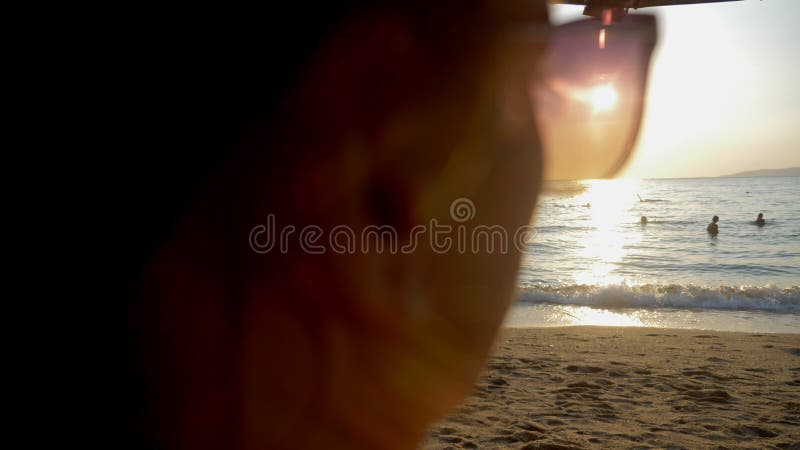 Por do sol ensolarado bonito no mar Vista através dos óculos de sol a mulher nos óculos de sol olha o por do sol no mar fotografia de stock royalty free Por do sol ensolarado bonito no mar Vista através dos óculos de sol a mulher nos óculos de sol olha o por do sol no mar fotografia de stock royalty free