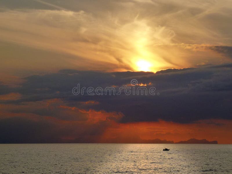 Por do sol espetacular com céu e as nuvens vermelhos sobre o mar de Menorca na Espanha com a silhueta de um barco na reflexão bri fotografia de stock Por do sol espetacular com céu e as nuvens vermelhos sobre o mar de Menorca na Espanha com a silhueta de um barco na reflexão bri fotografia de stock