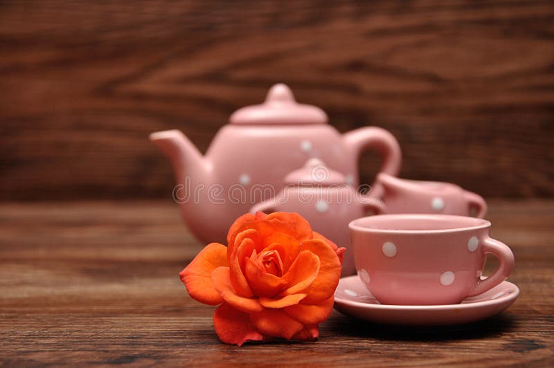 A porcelain spotted tea cup and kettle and an orange rose