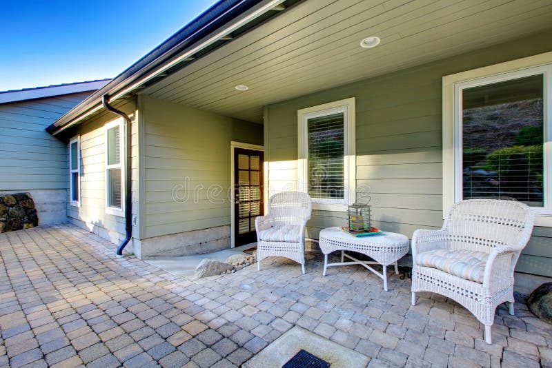 Back stoned porch with white wicker table set. Green paneled classic house. Back stoned porch with white wicker table set. Green paneled classic house