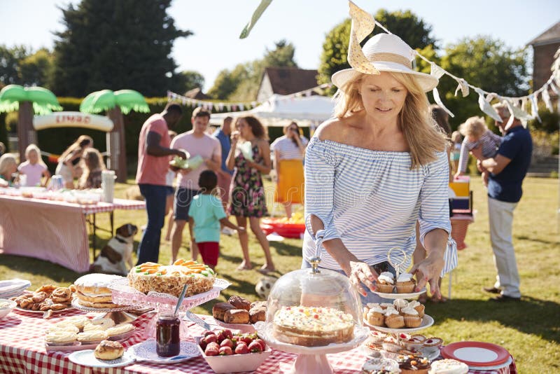 Porción madura de la mujer en parada de la torta en la fiesta ocupada del jardín del verano foto de archivo libre de regalías Porción madura de la mujer en parada de la torta en la fiesta ocupada del jardín del verano foto de archivo libre de regalías