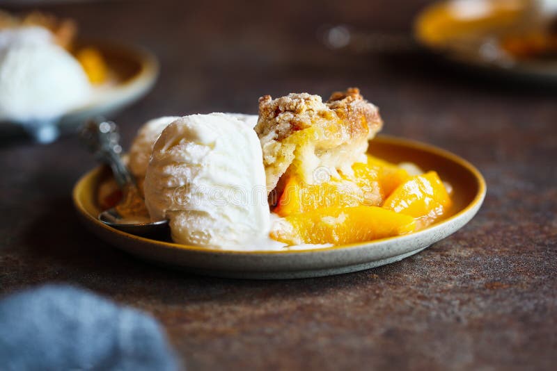 Freshly baked drop biscuit peach cobbler served with French vanilla ice cream over a dark rustic background. Freshly baked drop biscuit peach cobbler served with French vanilla ice cream over a dark rustic background