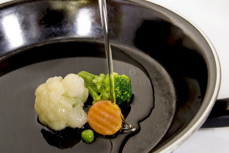 One black pan with vegetables and poring oil on top. One black pan with vegetables and poring oil on top.