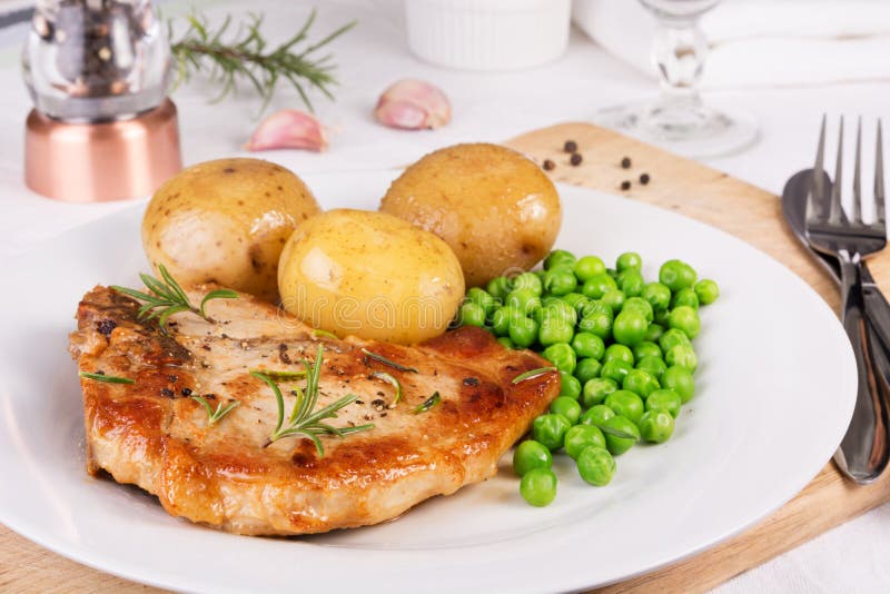 Pork chop, boiled jacket potatoes and green peas served on a plate