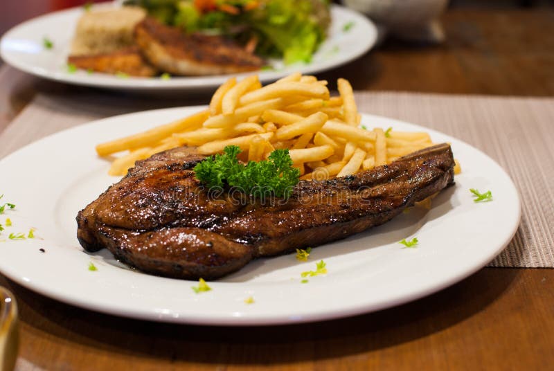 Pork Chop Grilled steak with French Fries, top with parsley.