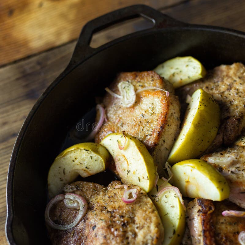 Pork chops with sliced onions and granny smith apples in a cast iron skillet.