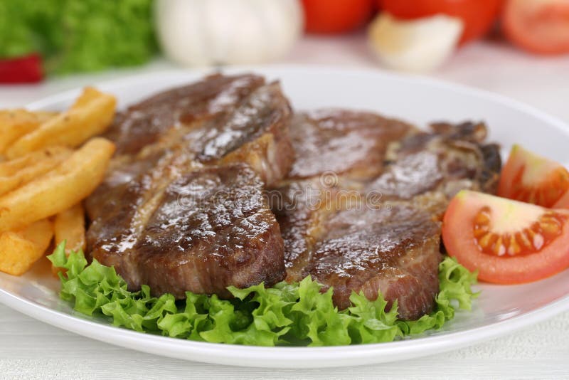 Pork chops steaks meal with fries, vegetables and lettuce on plate