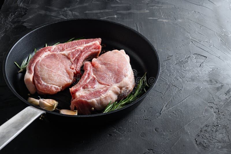 Pork rib chops in frying pan grill skillet with herbs, spices side view black stone bakground space for text vertical