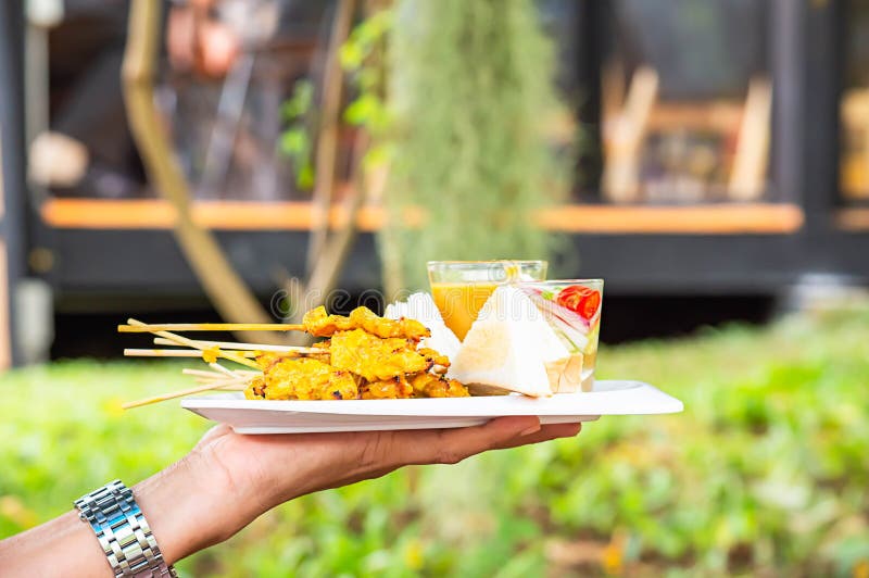 Pork Satay com leite de coco e pão com molho de amendoim estampado em prato de plástico branco na mão fotografia de stock royalty free
