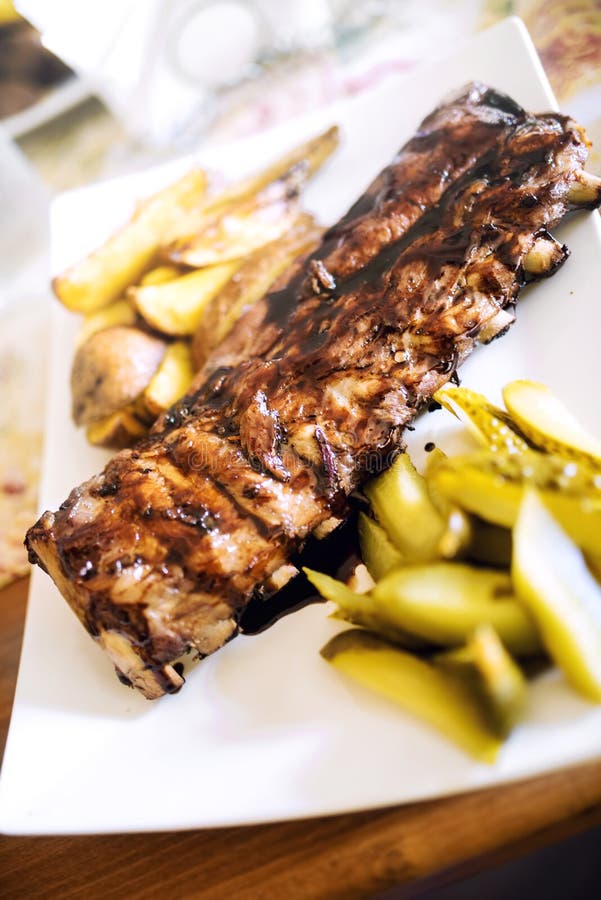 Pork spare ribs with barbecue sauce, golden potatoes and pickles. Main dish at restaurant, beef or pork delicacy stock image Pork spare ribs with barbecue sauce, golden potatoes and pickles. Main dish at restaurant, beef or pork delicacy stock image