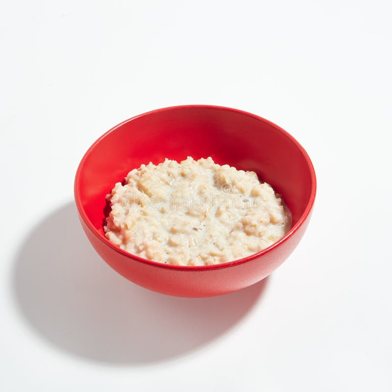 Porridge della farina d'avena con latte in ciotola rossa isolata su Backgro bianco fotografia stock libera da diritti Porridge della farina d'avena con latte in ciotola rossa isolata su Backgro bianco fotografia stock libera da diritti
