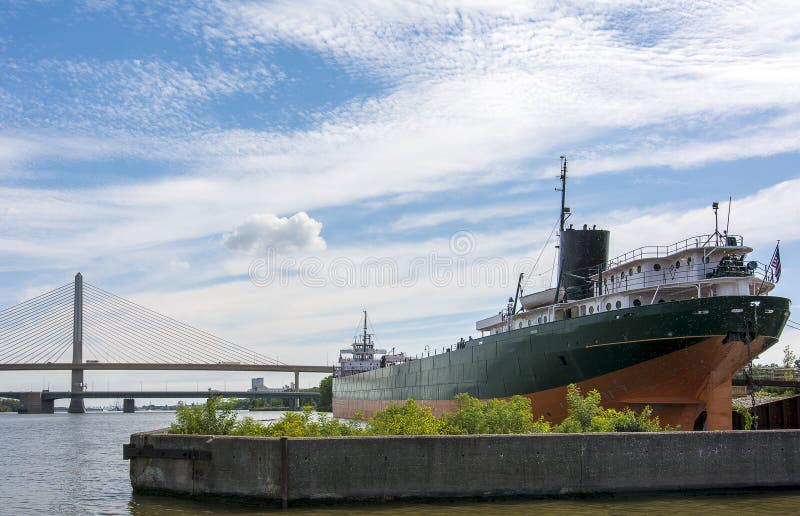 A cargo ship docked at the port of Toledo with the Veterans' Glass City Skyway bridge in Toledo Ohio in the background. A beautiful blue sky with white clouds for a backdrop. A cargo ship docked at the port of Toledo with the Veterans' Glass City Skyway bridge in Toledo Ohio in the background. A beautiful blue sky with white clouds for a backdrop.