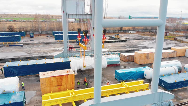Port de fret - Une grande grue industrielle transportant la cargaison dans les airs - des ouvriers en vêtements de travail brilla