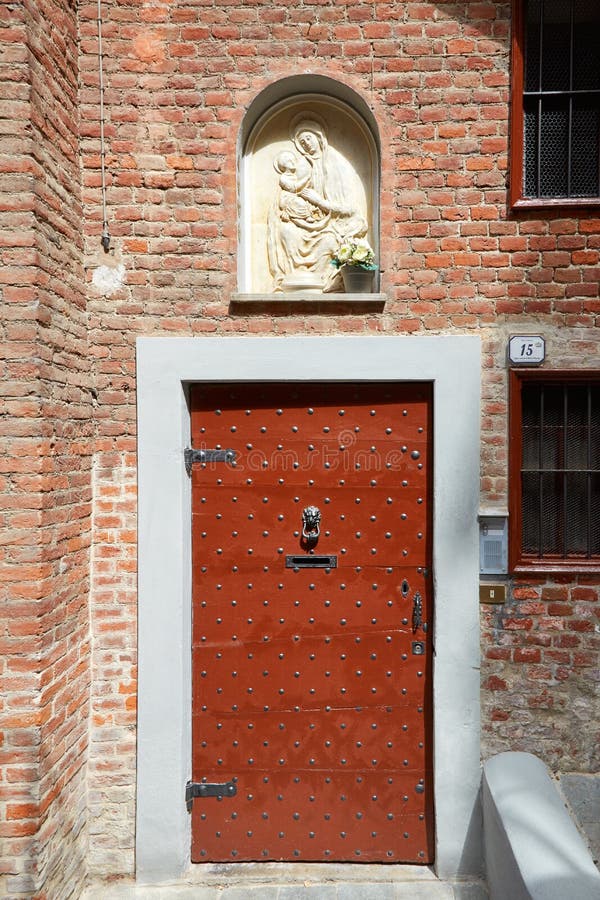 Porta di legno antica con i chiodi e bassorilievo di vergine Maria in un giorno soleggiato in Mondovi, Italia fotografia stock Porta di legno antica con i chiodi e bassorilievo di vergine Maria in un giorno soleggiato in Mondovi, Italia fotografia stock