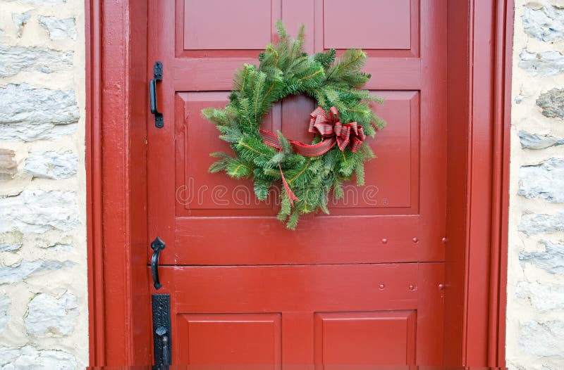 A view of a red, antique Dutch door with a simple pine bough Christmas wreath. A view of a red, antique Dutch door with a simple pine bough Christmas wreath.