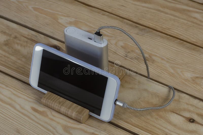 Portable charger charges a smartphone on a wooden table. Mobile phone mockup with dark screen and power bank