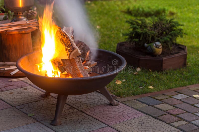 A portable fireplace with bright burning firewood making sparks and smoke at the backyard or garden near house. A place for eveni stock image A portable fireplace with bright burning firewood making sparks and smoke at the backyard or garden near house. A place for eveni stock image