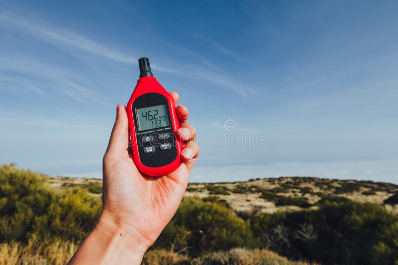 Portable thermometer in hand measuring outdoor air temperature and humidity stock photo