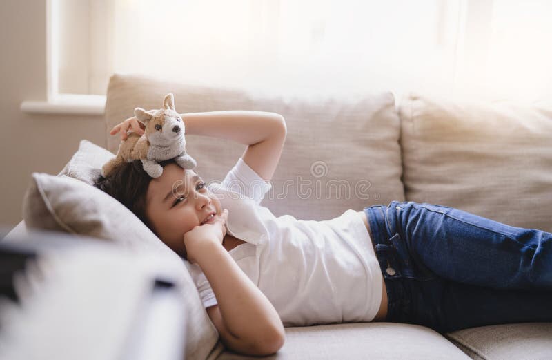 Portarit allegro ragazzo felice che guarda la telecamera con un sorriso sorridente bambino sdraiato sul divano che gioca con un ra fotografie stock