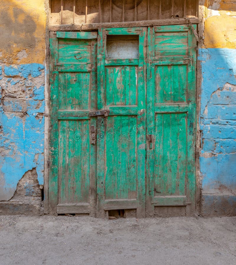 Closed green wooden grunge weathered abandoned door on dirty wall painted in yellow and blue colors. Closed green wooden grunge weathered abandoned door on dirty wall painted in yellow and blue colors