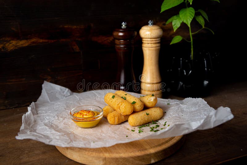 A portion of cheese sticks, served on a wooden board with mustard. Bar deep fried food. Shot in the interior of a bar against a stock photos A portion of cheese sticks, served on a wooden board with mustard. Bar deep fried food. Shot in the interior of a bar against a stock photos