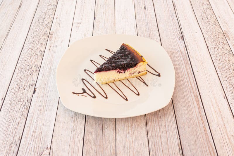 Portion of cheesecake with lots of red fruit jam and garnished with chocolate syrup on a white plate