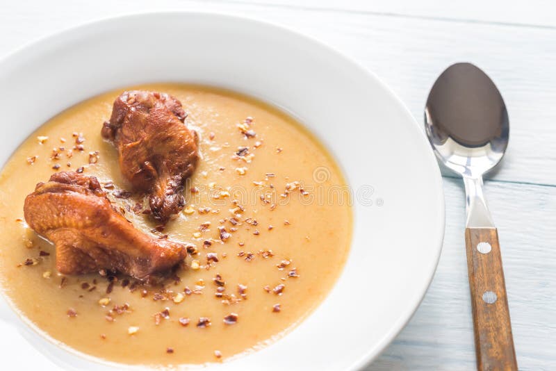 Portion of pea cream soup with smoked chicken wings.
