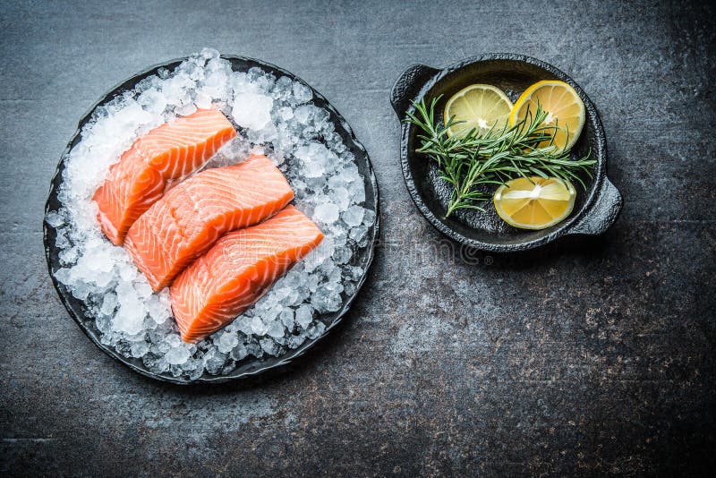 Portioned raw salmon fillets in ice on plate with lemon and rosemary