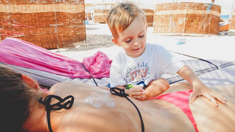 Portr?t der jungen Mutter liegend auf sunbed am Strand w?hrend ihr Kindersohn, der sie eine Massage macht lizenzfreie stockfotografie Portr?t der jungen Mutter liegend auf sunbed am Strand w?hrend ihr Kindersohn, der sie eine Massage macht lizenzfreie stockfotografie