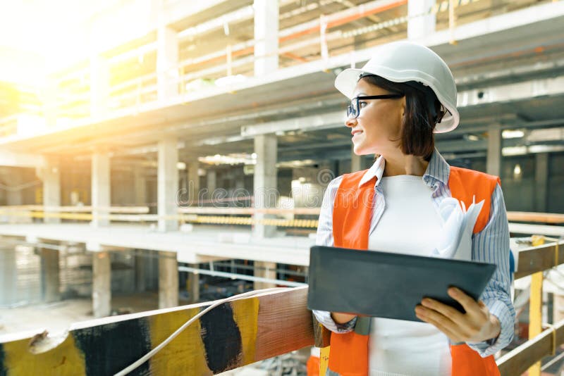 Portrait of adult female builder, engineer, architect, inspector, manager at construction site. Woman with plan, digital tablet stock photo