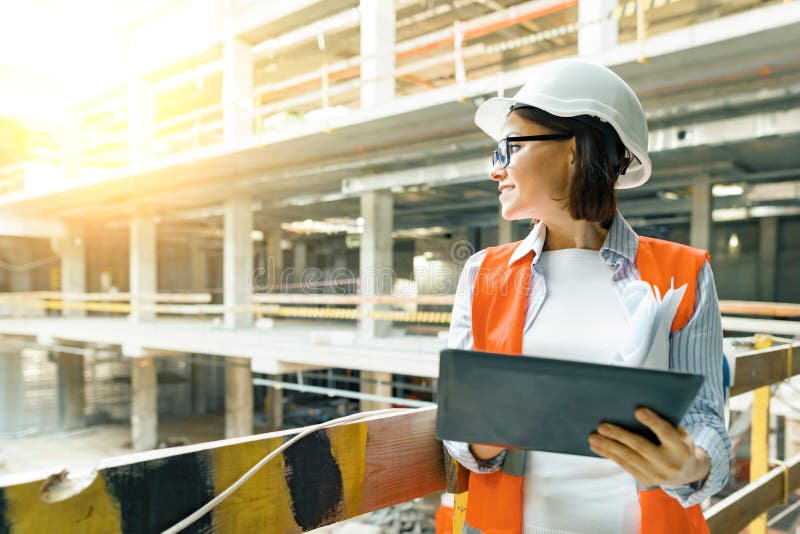 Portrait of adult female builder, engineer, architect, inspector, manager at construction site. Woman with plan, digital tablet