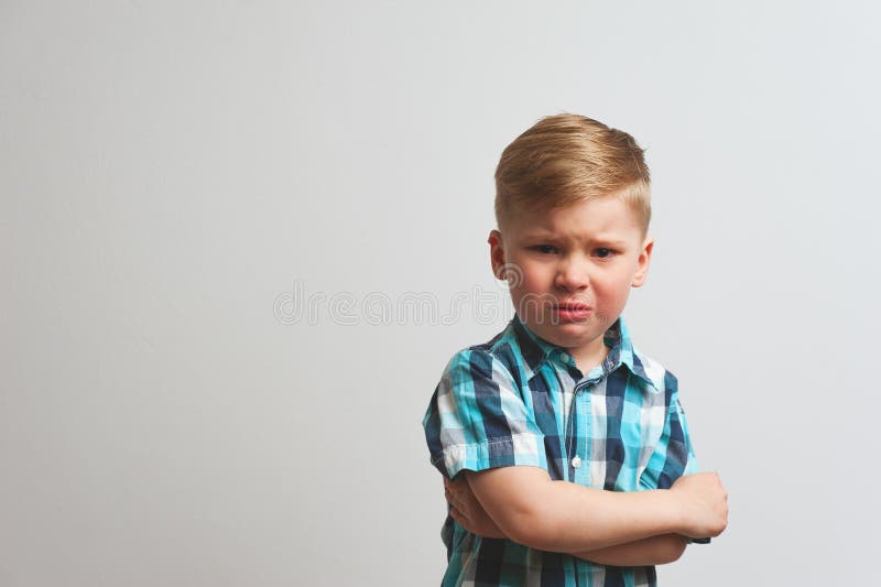 Unhappy crying caucasian boy staying with arms crossed on chest and looking at camera. Emotional portrait of little angry child. Unhappy crying caucasian boy staying with arms crossed on chest and looking at camera. Emotional portrait of little angry child.
